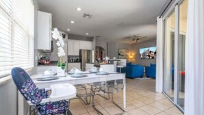 Una cocina moderna con armarios blancos, un comedor con mesa y sillas, y una sala de estar con sofás azules.
