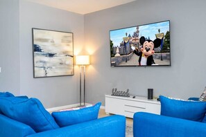 Sala de estar com televisão de tela plana, um quadro, um abajur e sofás azuis.