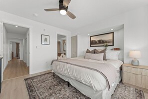 Quarto com cama, mesa de cabeceira, abajur e ventilador de teto.