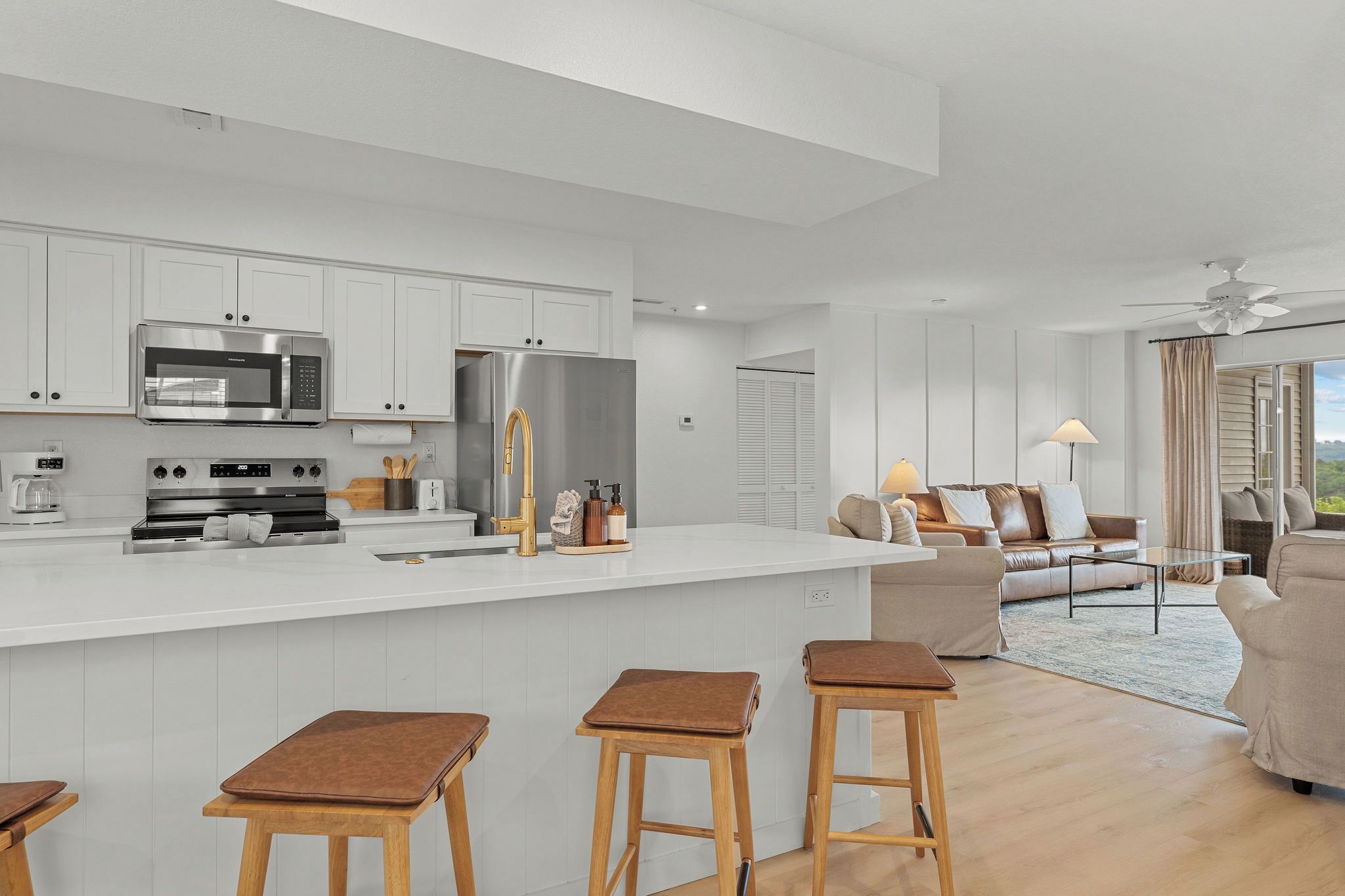 A modern kitchen with white cabinetry, stainless steel appliances, and a central island with stools.