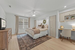 Un dormitorio con una cama, un escritorio, una silla, un televisor y una ventana con cortinas.