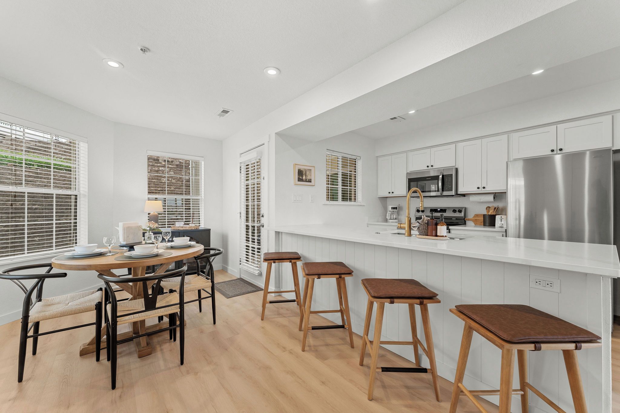 A modern kitchen with white cabinetry, stainless steel appliances, and a dining area with wooden stools.