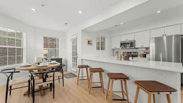 A modern kitchen with white cabinetry, stainless steel appliances, and a dining area with wooden stools.