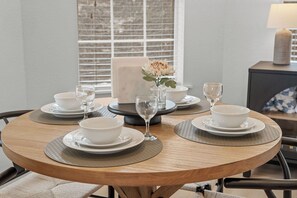 A round dining table with white plates, bowls, and wine glasses, set with a vase of flowers.