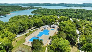 Oversigtsbillede af et resort med en stor swimmingpool omgivet af frodig vegetation og en sø.