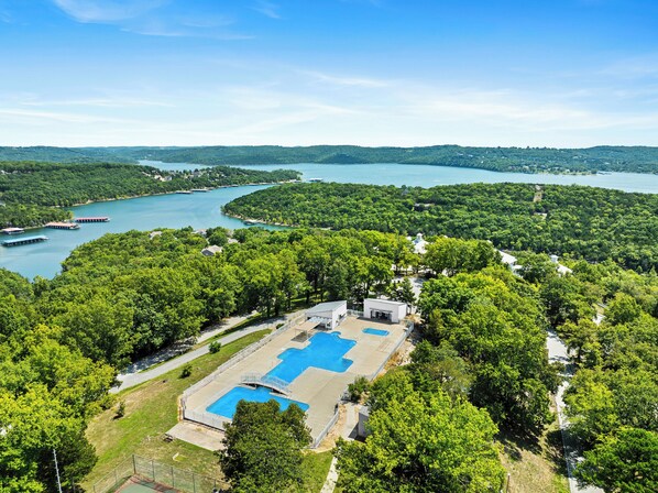 An aerial view of a resort with a large swimming pool surrounded by lush greenery and a lake.