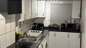 Une cuisine avec des meubles blancs, un plan de travail noir, un four à micro-ondes, un grille-pain et un évier.