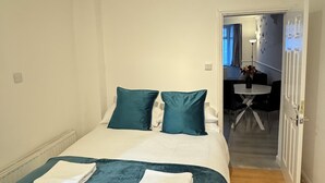 Un lit bien fait, avec une couette bleue et blanche, deux coussins turquoise et deux serviettes blanches pliées.