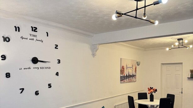 Un salon moderne avec un canapé d’angle, un coin repas comprenant une table et des chaises, et une horloge murale.