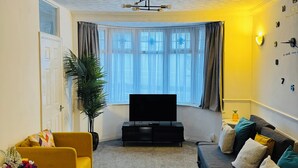 Un salon comprenant un téléviseur, un canapé et un fauteuil, une plante en pot et une horloge murale.
