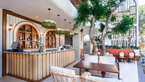 Una zona de bar con mostrador, sillas de mimbre, una mesa y un árbol.