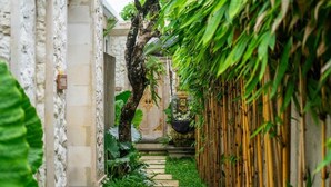 Un estrecho sendero de piedra bordeado de abundante vegetación y bambú, que conduce a la entrada de un edificio tradicional.