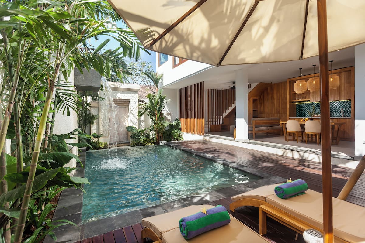 Un espace piscine doté de chaises longues, d’une cascade et d’un coin repas avec des meubles en bois.