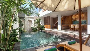 A pool area with lounge chairs, a waterfall feature, and a dining area with wooden furniture.