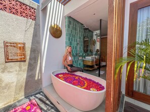Una mujer sentada en una bañera llena de flores de colores, con un letrero con las normas de la piscina en la pared.
