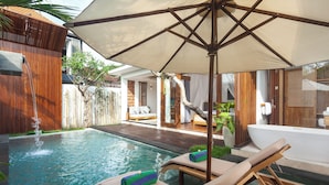 Un área junto a la piscina con sillones de descanso, una sombrilla grande y una bañera de hidromasaje.