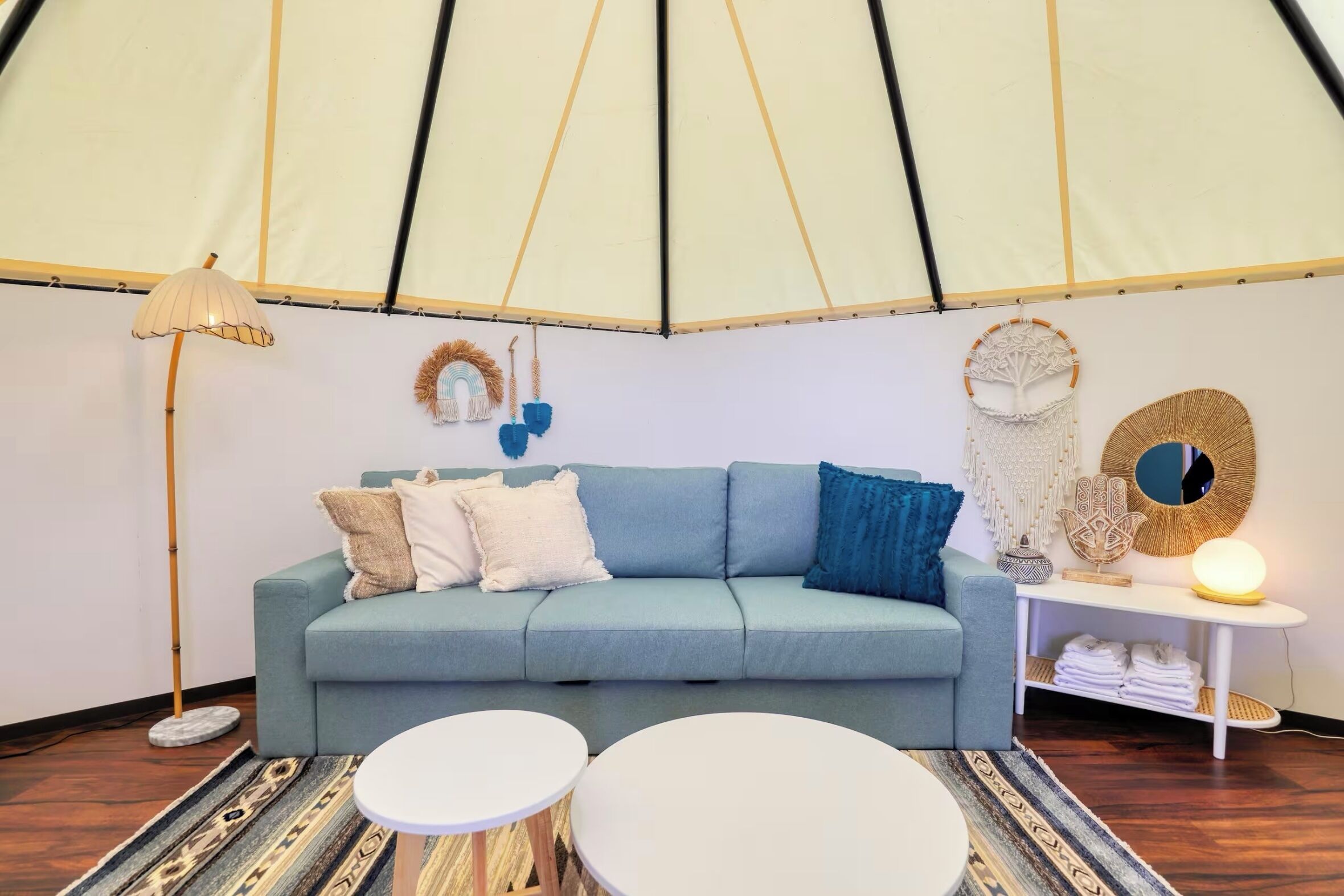 Ein Zeltraum mit einem hellblauen Sofa, zwei runden Tischen, einer Stehlampe und Wanddekorationen.