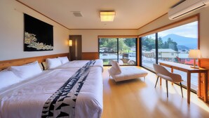 A modern hotel room with a large bed, a sofa, a desk, and a view of the outdoors. - Retreat Camp Mahoroba (Fujikawaguchiko)