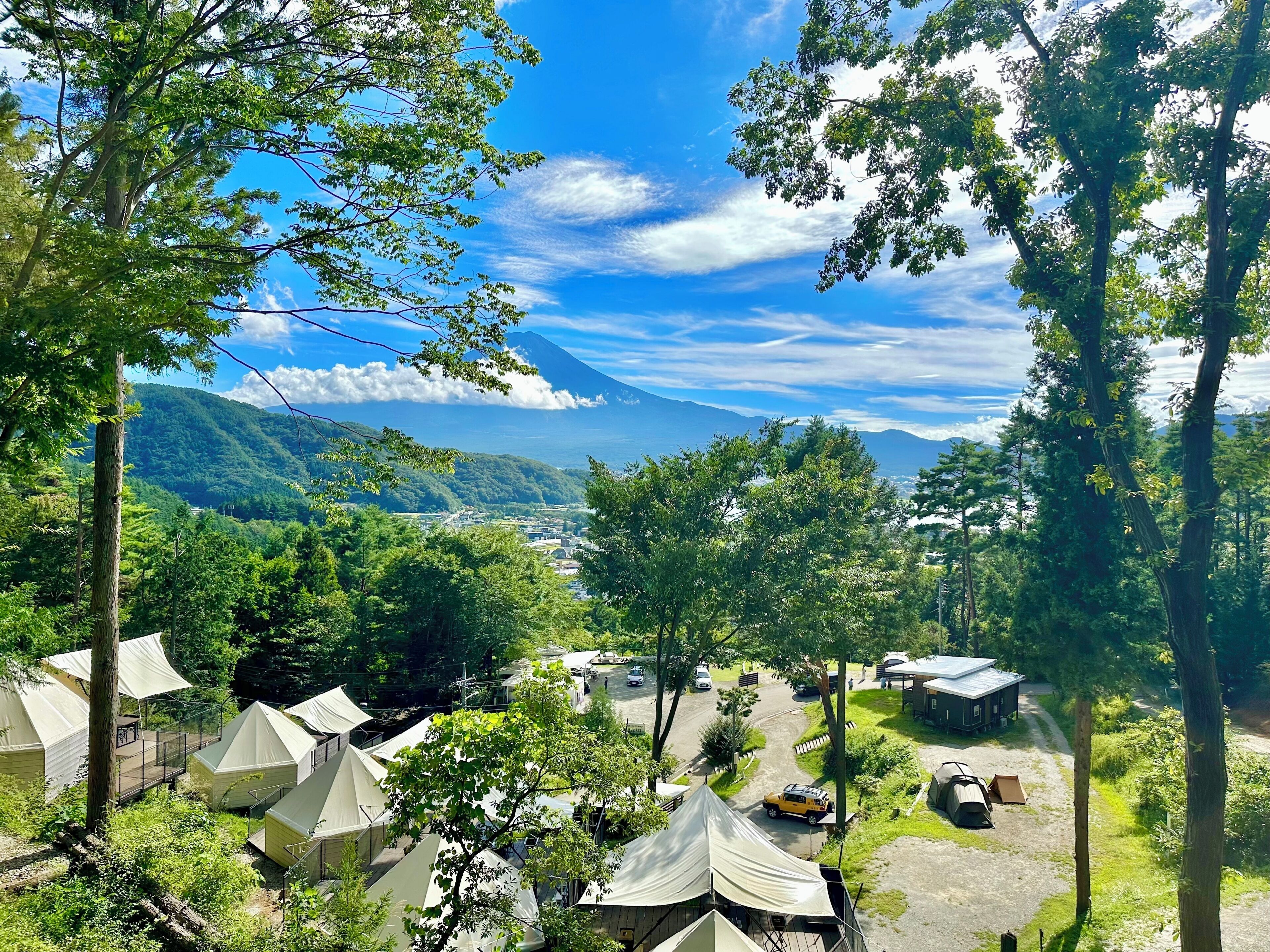 A campsite with multiple tents, surrounded by lush greenery and a mountainous backdrop.