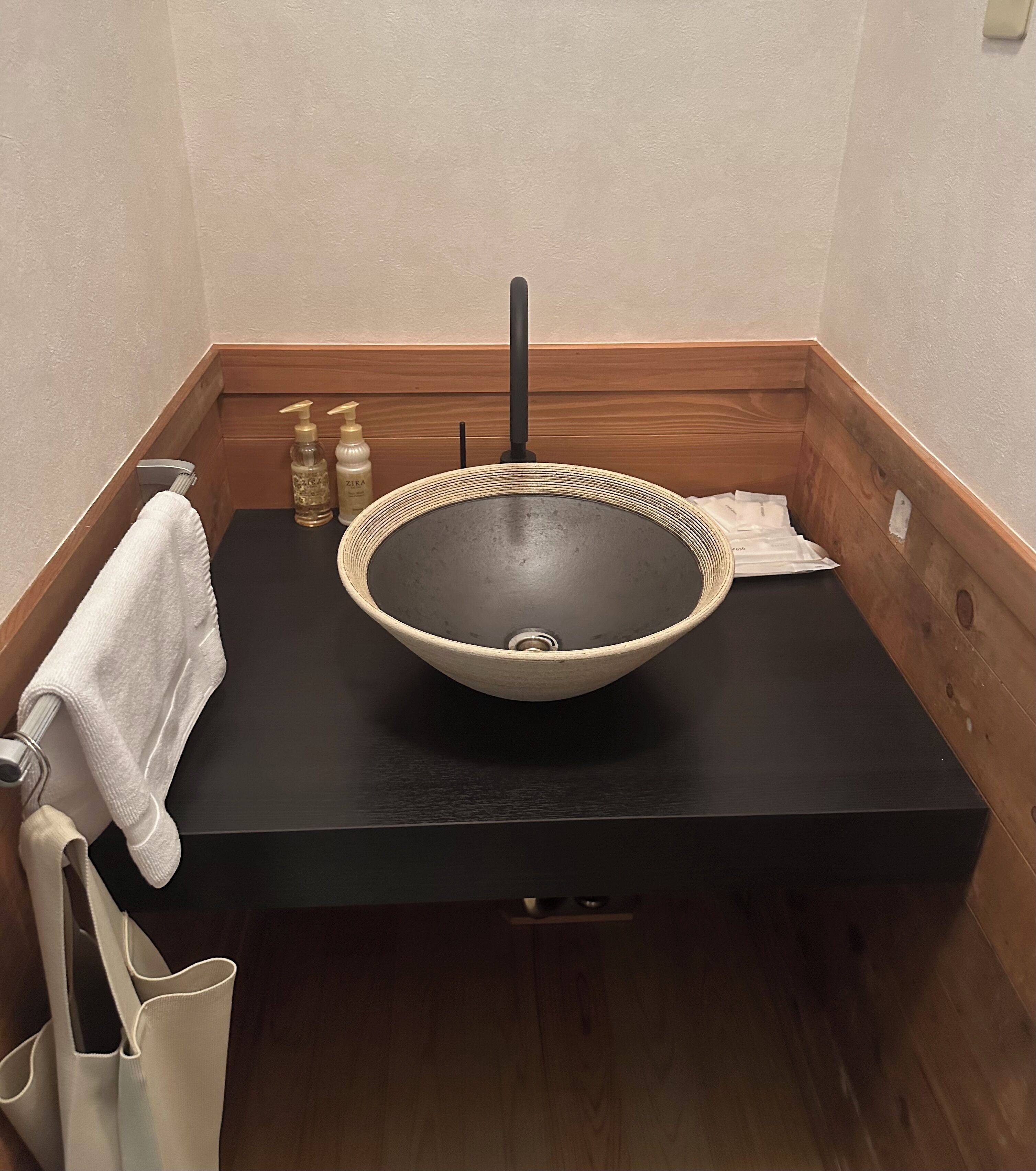 Un baño con encimera negra, lavabo de cesta trenzada y toallero.
