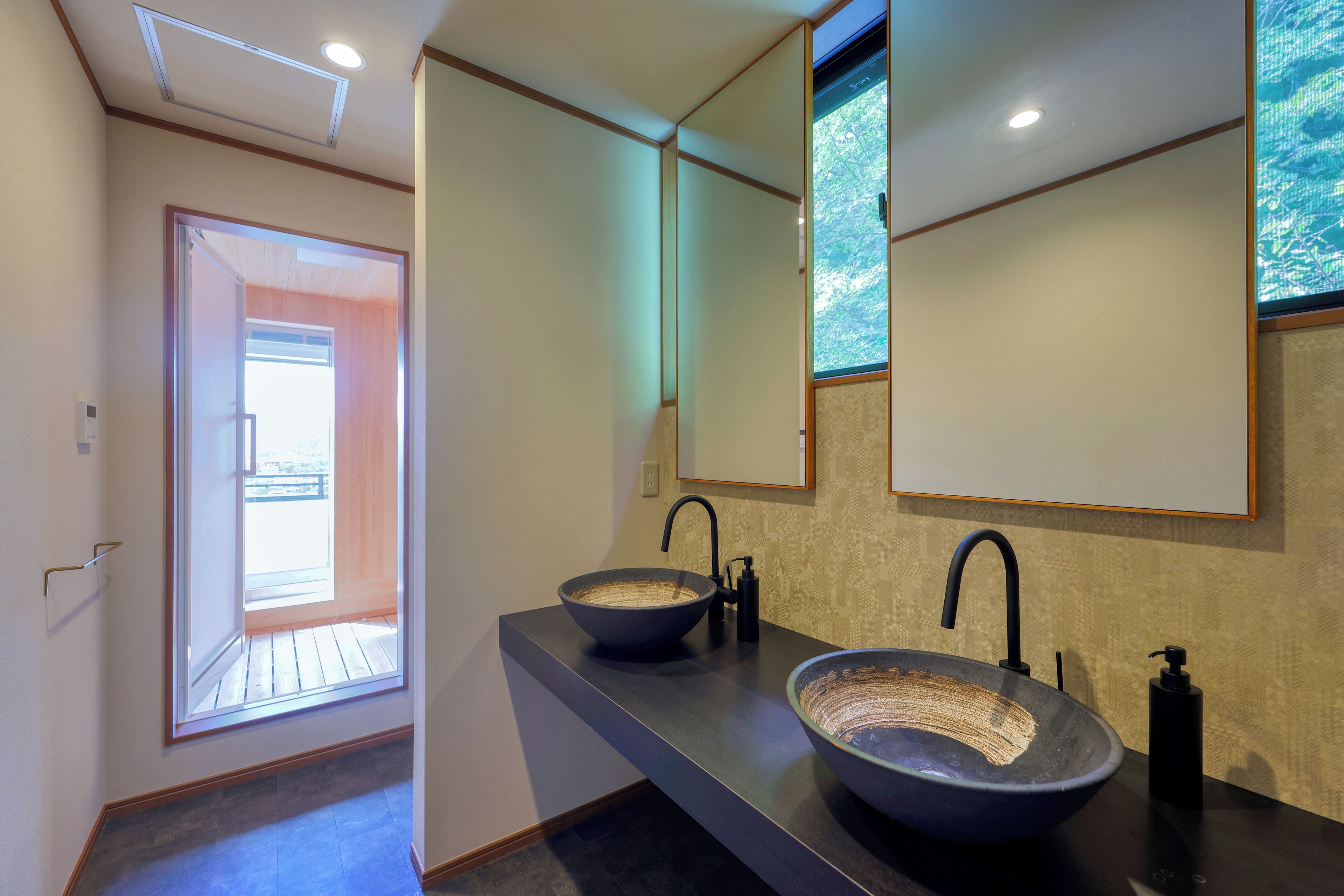 A modern bathroom with two large vessel sinks, a large mirror, and a view of the outdoors through a door.