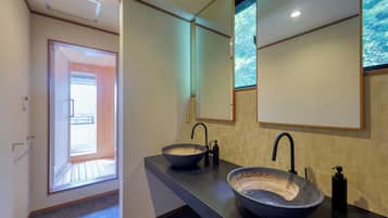 A modern bathroom with two large vessel sinks, a large mirror, and a view of the outdoors through a door.