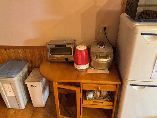 Una kitchenette con una tostadora, una cocedora de arroz y un microondas sobre una mesa de madera.