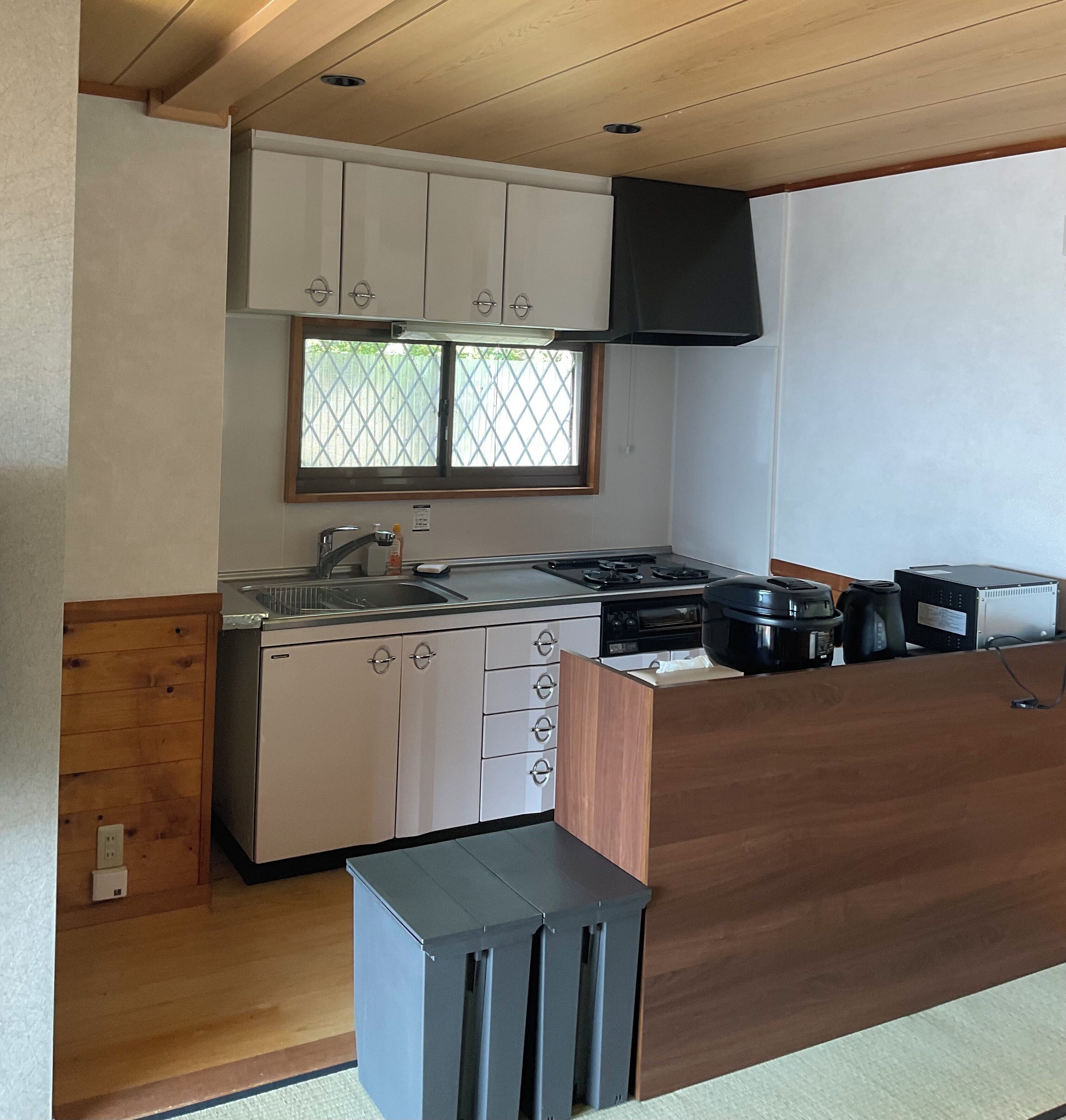 Cocina compacta con armarios blancos, estufa, pileta y ventana con vista a la vegetación.