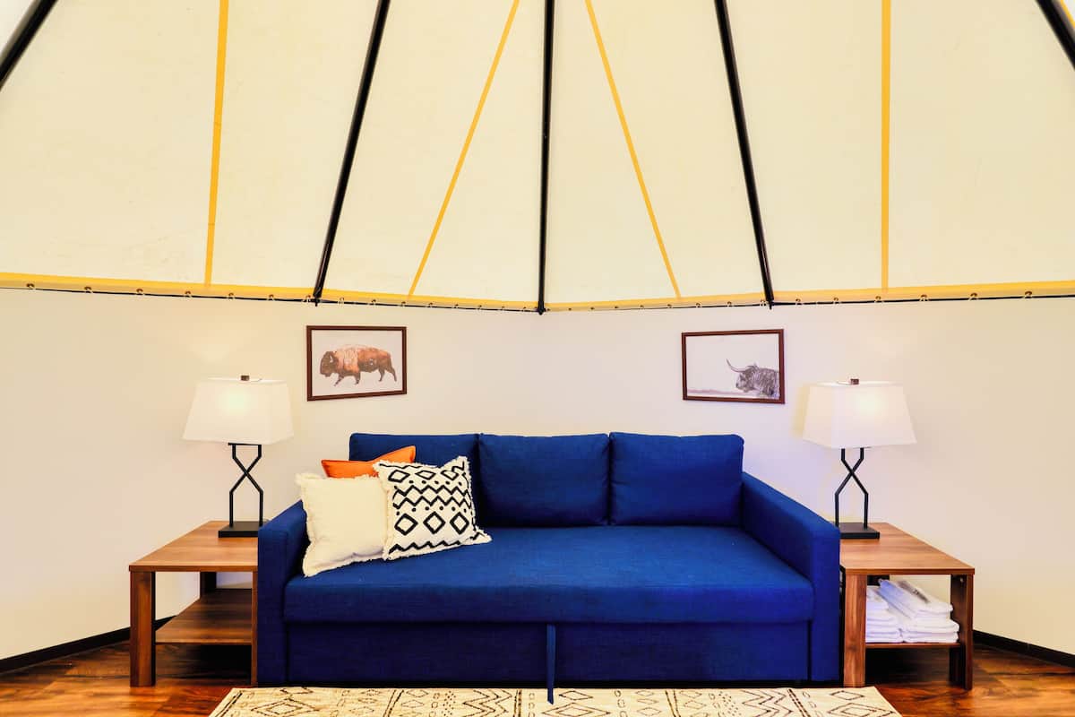 A cozy room with a blue sofa, two side tables with lamps, and framed pictures on the wall.