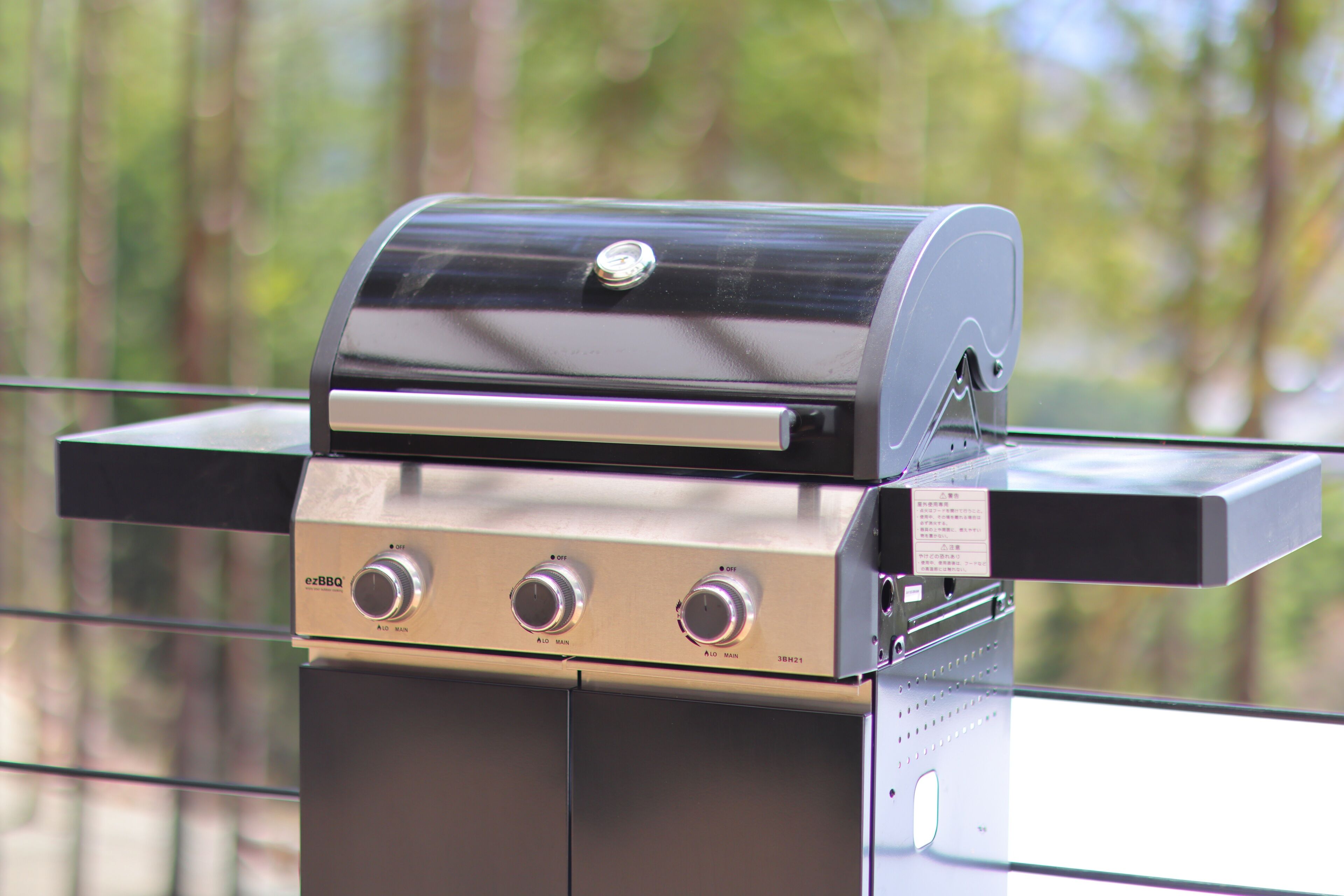 Un barbecue doté d’un écran numérique et de boutons de contrôle, fixé sur une rambarde et offrant une vue sur les arbres en arrière-plan.