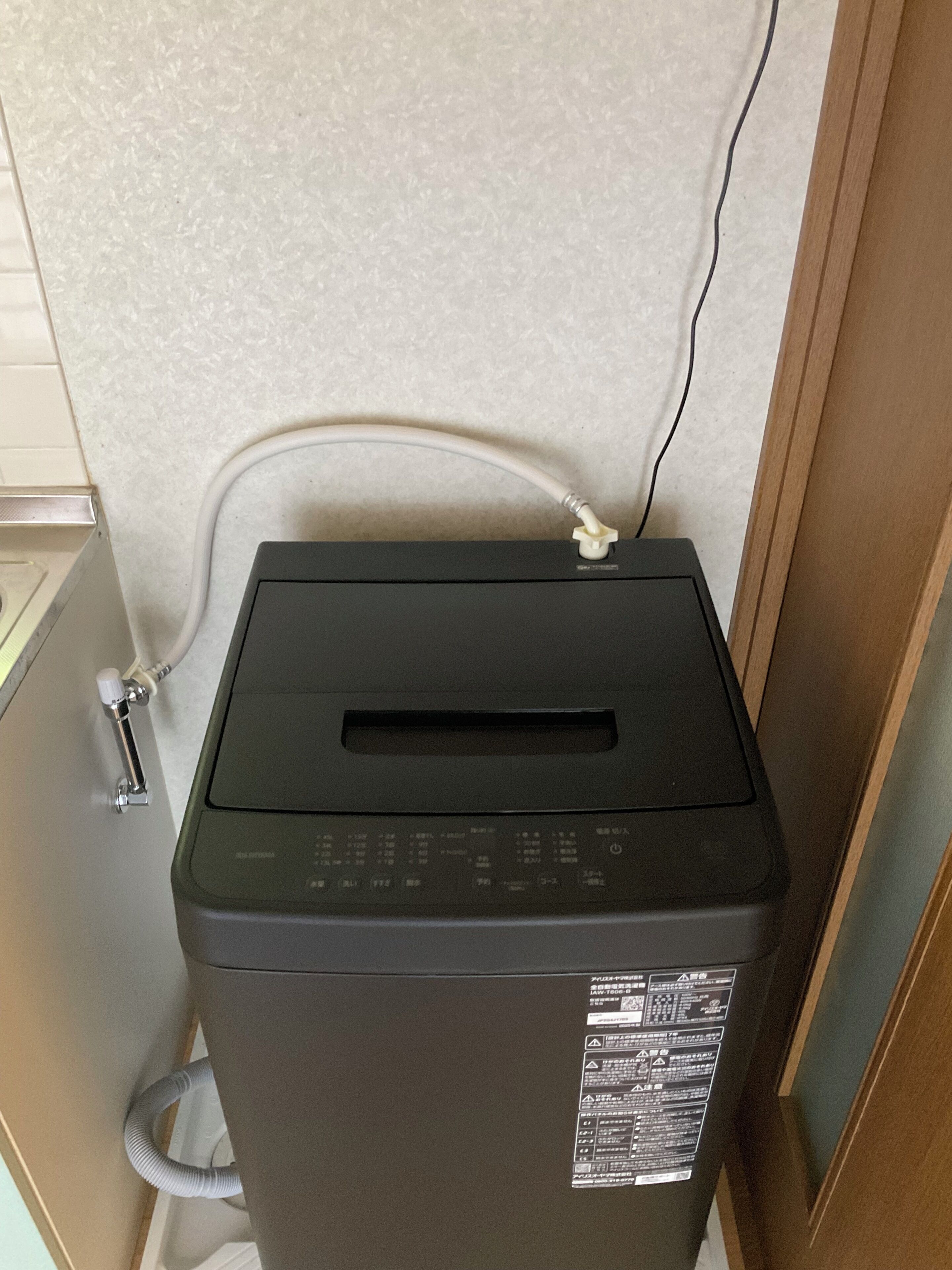 A compact, dark-colored trash bin with a slot for inserting coins, a hose attached to the side, and a label with safety instructions.