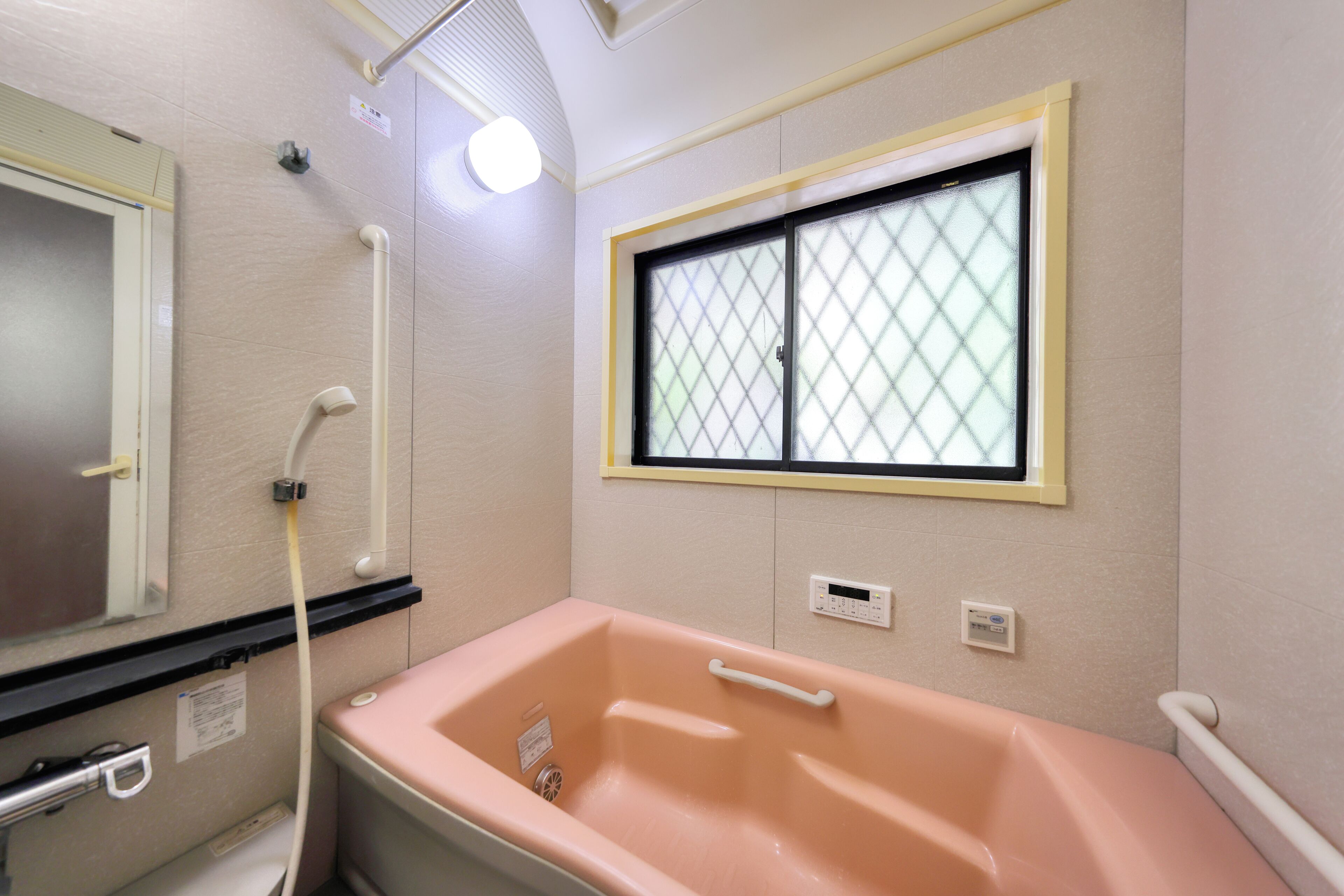 Une salle de bain avec une baignoire rose, une fenêtre à carreaux, un miroir et un panneau de commande de la douche.