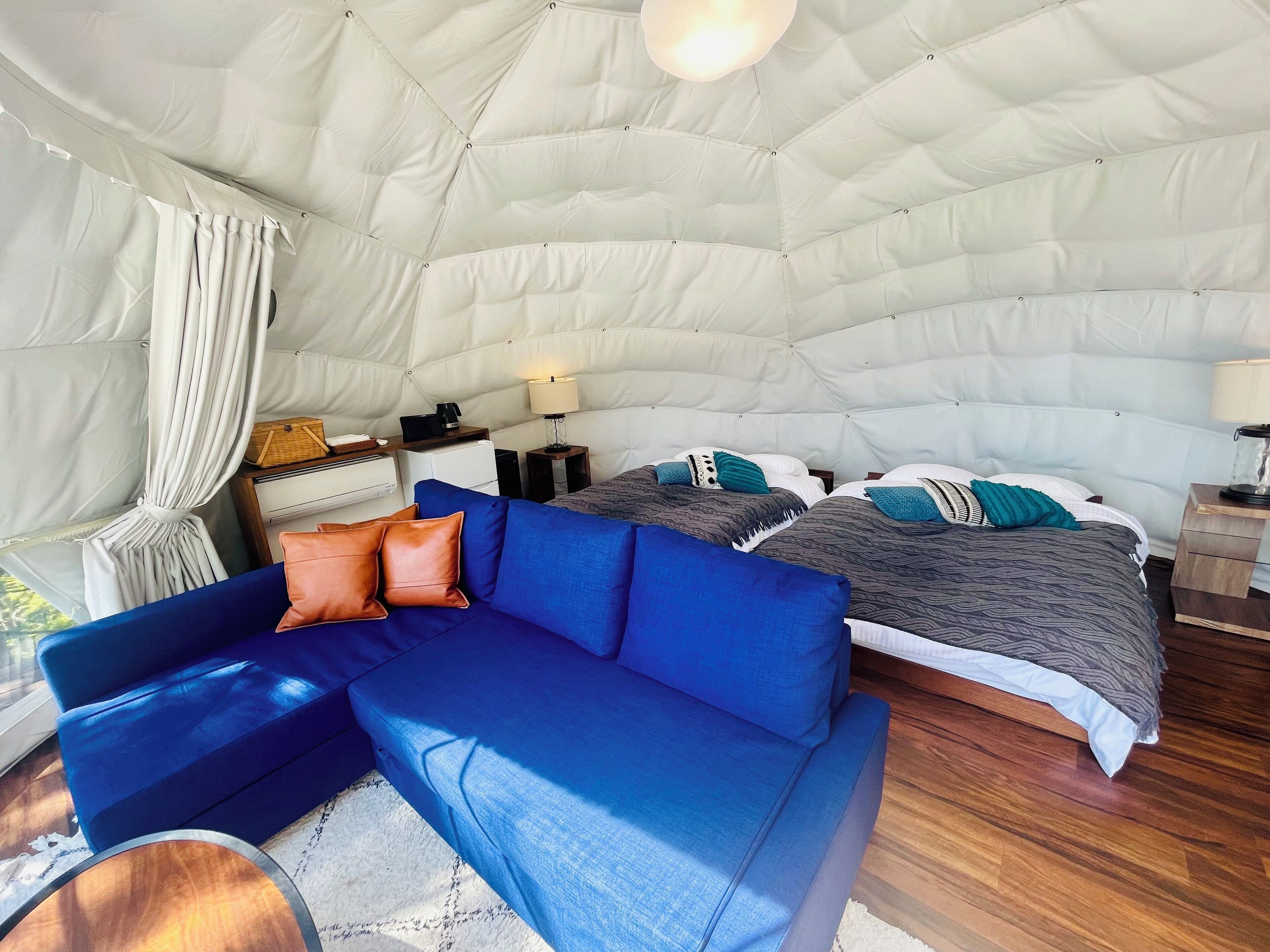 Un intérieur chaleureux avec un canapé bleu, un lit recouvert d’une literie à motifs et une structure de plafond blanche en forme de tente.