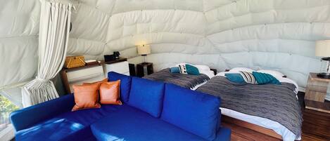 Un intérieur chaleureux avec un canapé bleu, un lit recouvert d’une literie à motifs et une structure de plafond blanche en forme de tente.