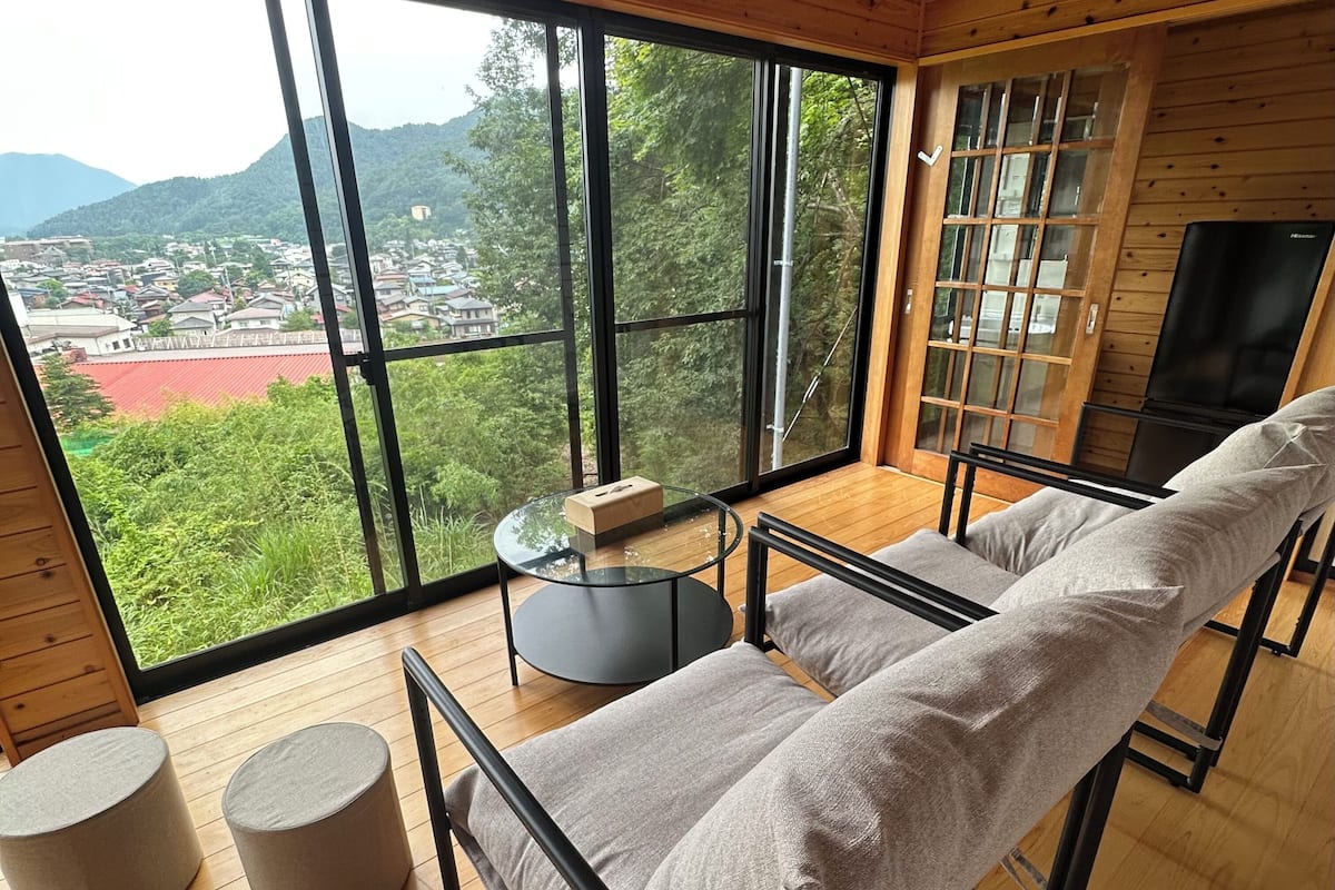 A modern room with a large window, a sofa, a small table, and two ottomans.