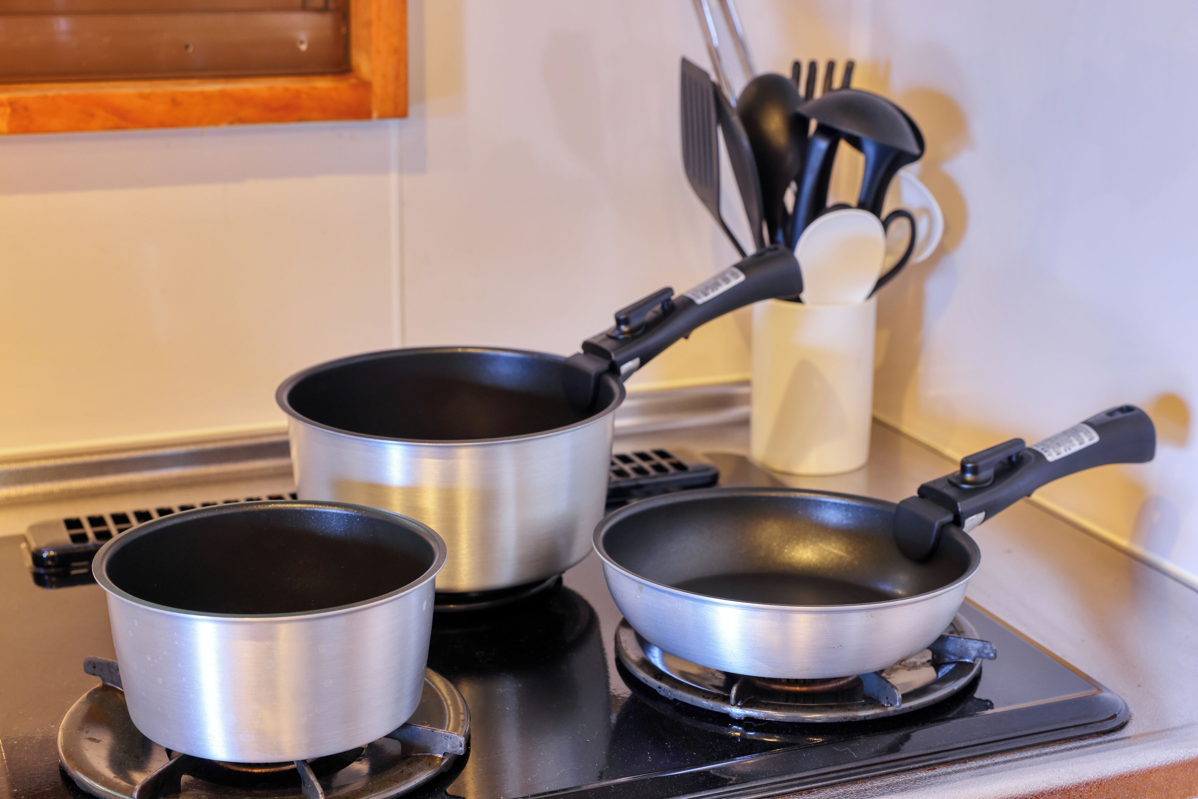 Two stainless steel pots on a stove, a white utensil holder with black utensils, and a wooden cabinet in the background.