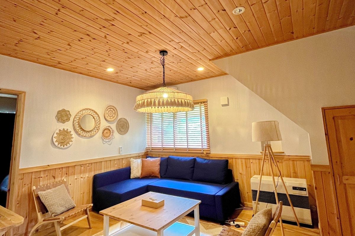 A spacious living room with a wooden ceiling, a blue sofa, a white coffee table, and a patterned rug.