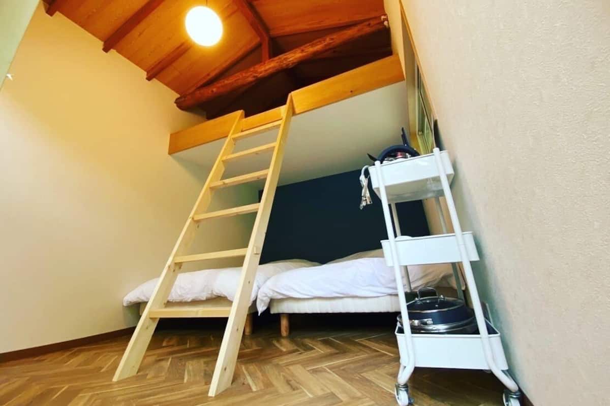 A small, cozy room with a wooden loft bed, a white ladder, and a white shelf unit.