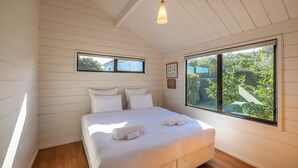 A bedroom with a large window, wooden walls, and a bed with white linens and towels. - Matai Cottage in Oneroa with Sea Views (Waiheke Island)