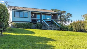 A two-story house with a balcony, a staircase, and a well-maintained lawn. - Matai Cottage in Oneroa with Sea Views (Waiheke Island)