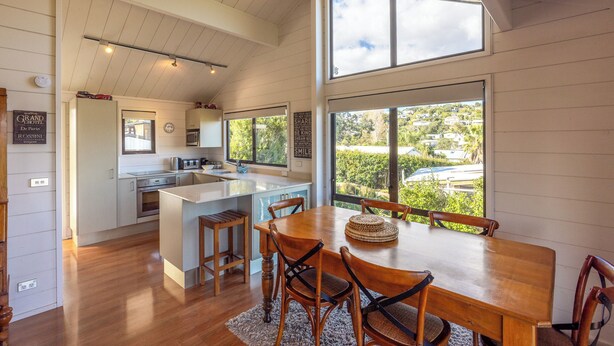 A spacious kitchen with wooden cabinets, a central island, and a large window offering a view of the surrounding area. - Matai Cottage in Oneroa with Sea Views (Waiheke Island)