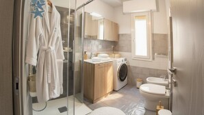 A modern bathroom with a glass shower enclosure, a washing machine, a sink, and a toilet. - Comfort and Relax in the Heart of Imperia | Ap44 (Imperia)