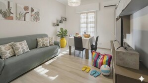 A modern living room with a grey sofa, a dining table with chairs, a yellow plant, and a TV on a stand. - Comfort and Relax in the Heart of Imperia | Ap44 (Imperia)