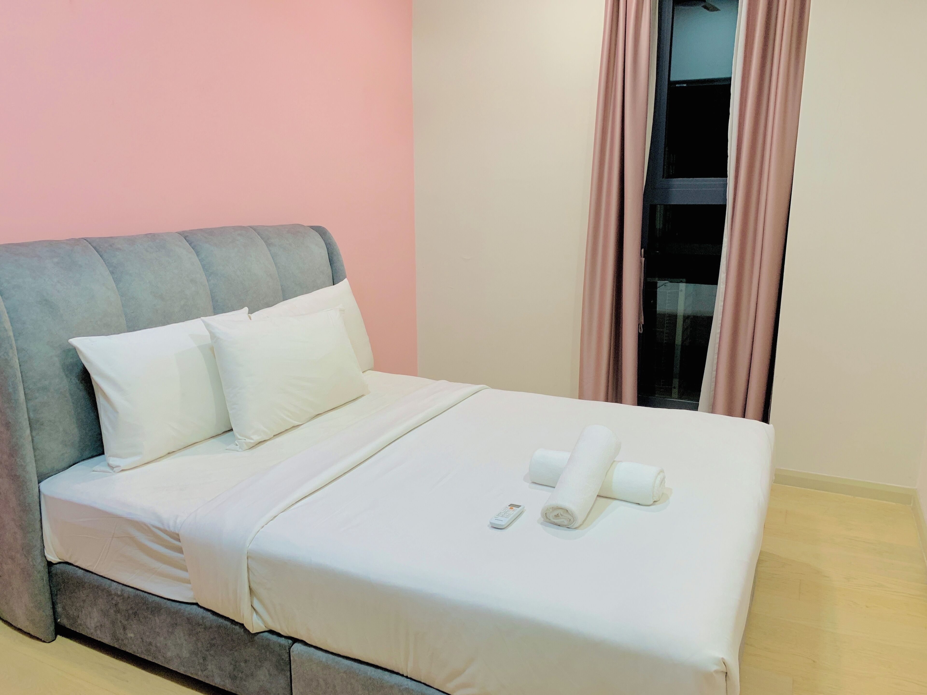 A neatly made bed with pillows and rolled towels, a remote control, and a window with curtains.