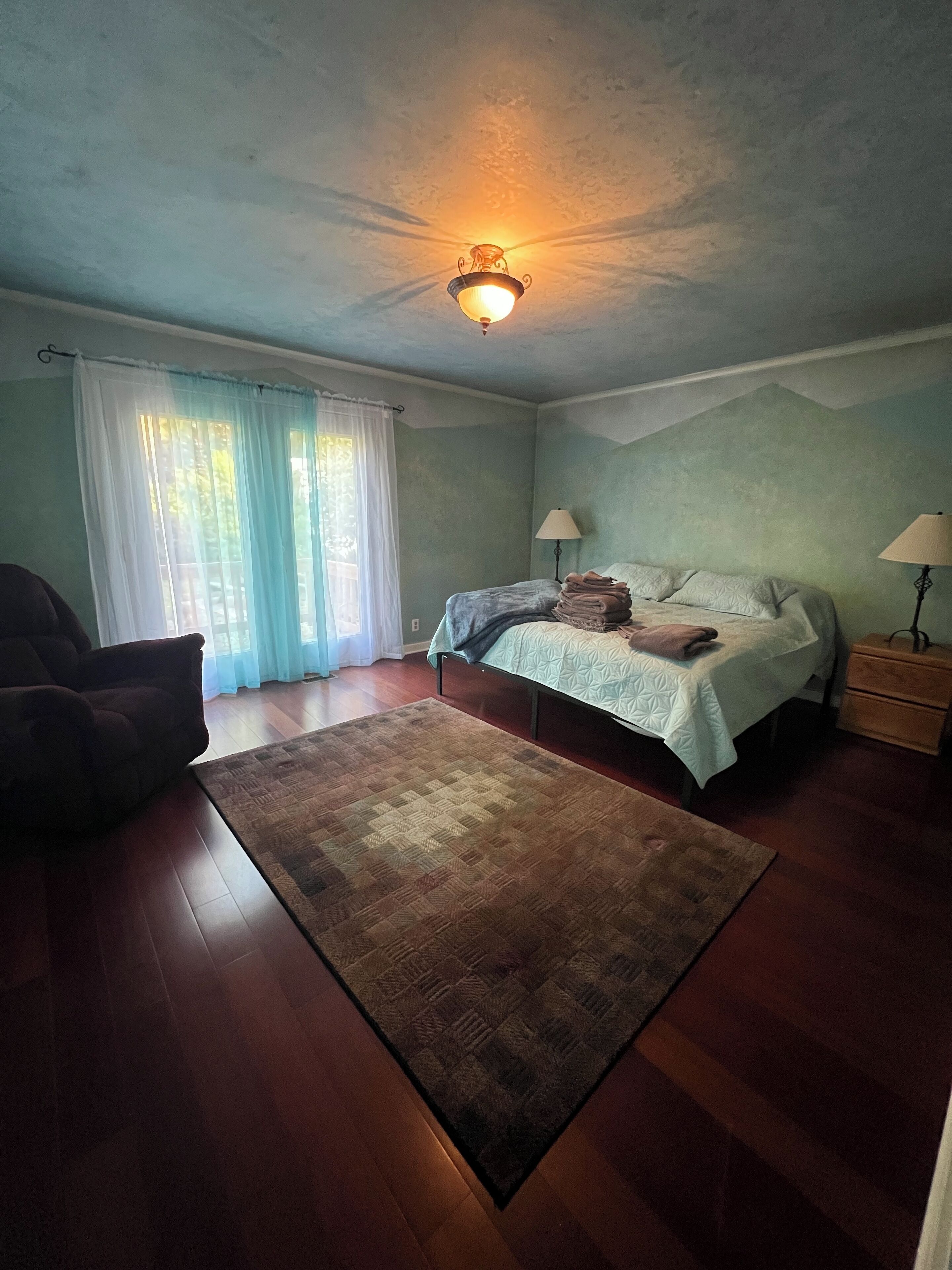 Una camera da letto con un letto, due comodini, una sedia, un tappeto e una lampada a soffitto.