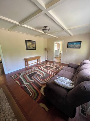 Un salon avec un canapé marron, un tapis à motifs, un banc en bois et un ventilateur de plafond.