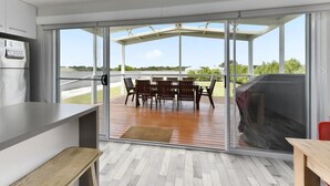 Et moderne køkken med en skydedør, der fører til en udendørs patio med træterrasse og spisebord.