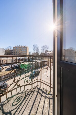 A balcony with a metal railing overlooking a parking area with several cars, including a green one. - Spacious and sunny apartment (Riga)