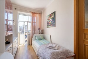A small bedroom with a bed, a window with curtains, a painting on the wall, and a wooden door. - Spacious and sunny apartment (Riga)