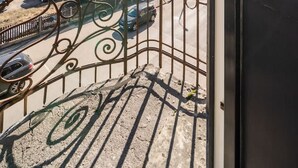Un balcon doté d’une balustrade en métal donnant sur un parking où sont garées plusieurs voitures, dont une verte.